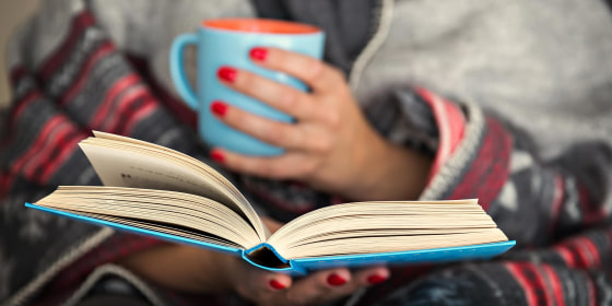 Woman holding a coffee mug and reading a popular memoirs, selected by Goodreads