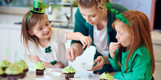 Mother and her daughters wearing St. Patricks Day decor and decorating cupcakes