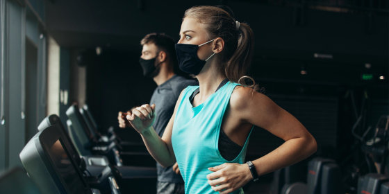 Woman and Man running on treadmills at the gym while wearing breathable face masks