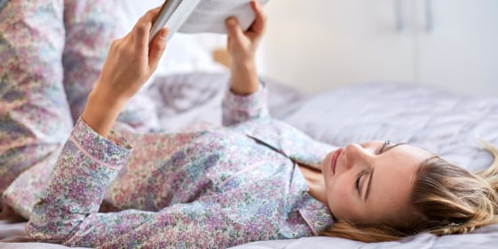 Woman laying in her bed reading a book, wearing a pink matching pajama set