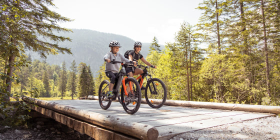 Mother and daughter riding bikes with helmets, through a scenic outdoor path