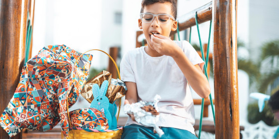 Little boy with glasses, eating chocolate out of a packaged Easter Basket