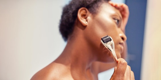 Close-up image of a woman microneedling her face with a gold and black roller