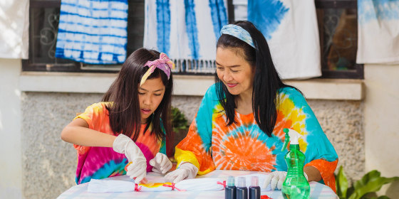 Woman and her daughter, wearing tie dye, tie dying with a kit outside their house