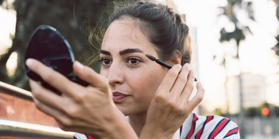 Woman looking into compact mirror brushing her brows