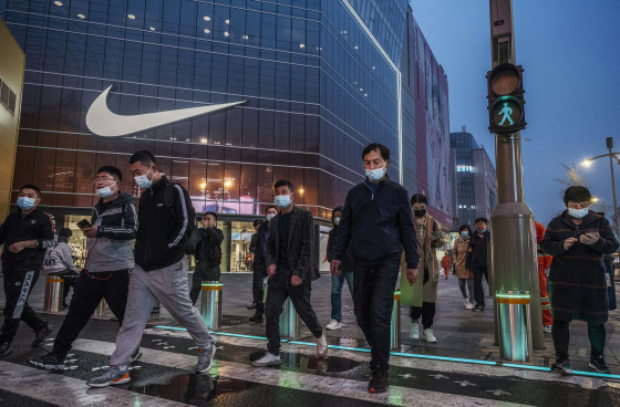 Image: People cross a street in front of a Nike store at a shopping area on March 26, 2021 in Beijing, China.