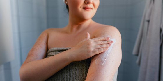 Woman in a towel, in her bathroom, rubbing lotion on her arm