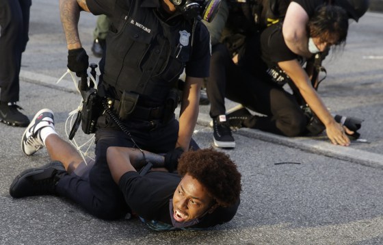 Image: Protestors being detained by police officers.