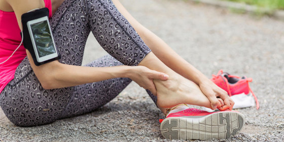 Woman sitting on the ground rubbing her foot out of her pink sneaker