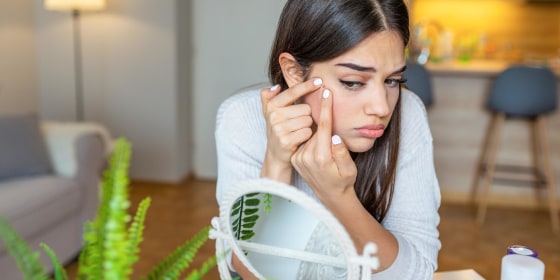 Woman squeezing pimples while looking at the mirror