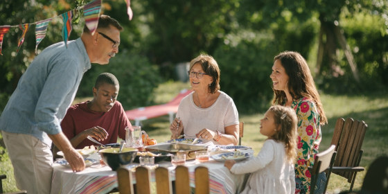 Senior man and granddaughter talking while having lunch with family in backyard during party