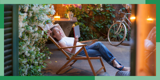 Woman relaxing on deck chair in backyard at dusk, reading on digital tablet