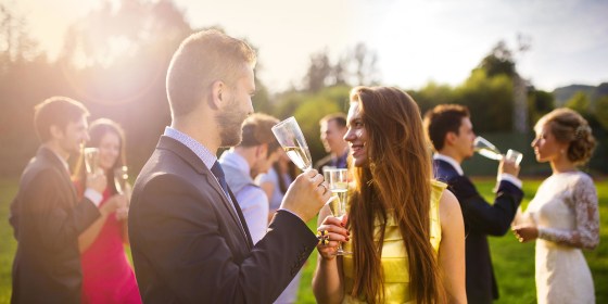Wedding guests clinking glasses while the newlyweds drinking champagne in the background