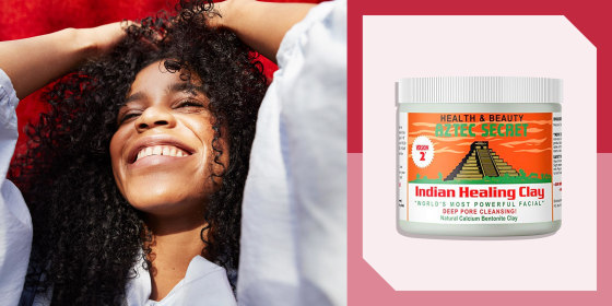 Close-up of young woman against red wall with curly hair and a bottle of Aztec Healing clay
