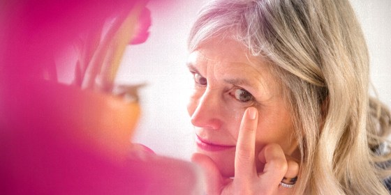 Woman applying cream to wrinkle near eye