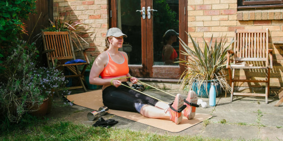 Woman sitting on a yoga may, exercising in her garden, using a resistance band