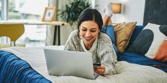 Shot of a young woman using a laptop and credit card on the bed at home