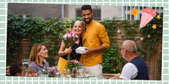 Happy young man with bouquet and gift hugging his senior mother in law outdoors in garden