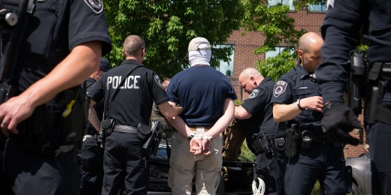 Image: Back of a person handcuffed being escorted by police officers.