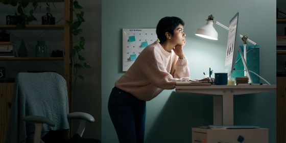 Young woman standing on desk using computer and working after hours at home office.