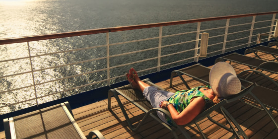 A middle aged woman in a sunbonnet relaxes on the top deck of a cruise ship during her vacation at sea