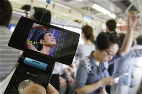 A man watches television on his mobile phone while commuting on a train in Tokyo
