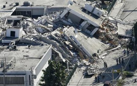 Haitians survey the damage to a building that collapsed onto a road in downtown Port-au-Prince