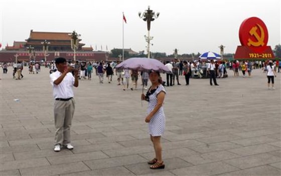 A giant Communist emblem is seen on display as a woman holding an umbrella poses for a photograph at Beijing's Tiananmen Square