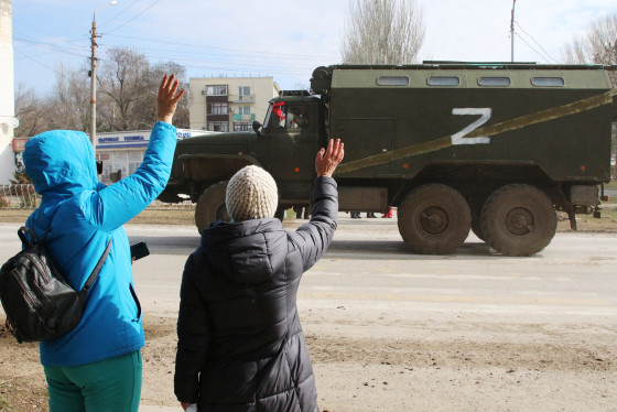 Image: People wave as a Russian Army military truck drives along a street in Armyansk