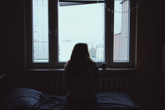 View Of Woman Looking Through Window At Home