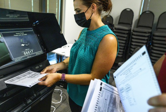 Election judges submit test ballots into a machine