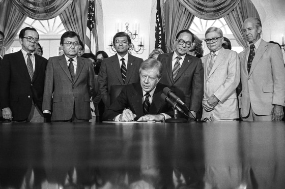 President Jimmy Carter signs a bill at the White House creating a commission to look into the wartime internment of Japanese Americans as Senator Daniel Inouye, D-Hawaii, Rep. Norm Mineta, D-Calif., Senator Spark Matsunaga, D-Hawaii, Rep. George Danielson, D-Calif., watch, on July 31, 1980.