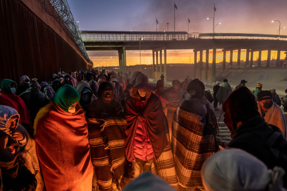 Migrants keep warm by a fire at dawn after spending a night alongside the U.S.-Mexico border fence on Dec. 22, 2022 in El Paso, Texas.