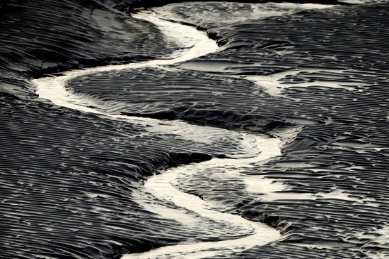 A channel flows through the mud flats along the Seward Highway and Turnagain Arm in Alaska on Oct. 25, 2014. Authorities said, a 20-year-old man from Illinois who was walking Sunday evening, May 21, 2023, on tidal mud flats with friends in an Alaska estuary, got stuck up to his waist in the quicksand-like silt and drowned as the tide came in before frantic rescuers could extract him.