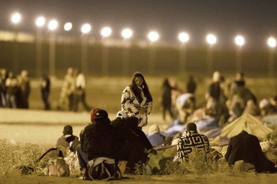 Migrants wait in the cold at a gate in the border fence in El Paso, Texas
