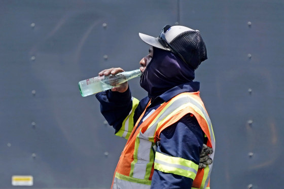 Standing in the mid-afternoon heat, a worker takes a drink during an asphalt resurfacing job in Richardson, Texas, on June 20, 2023.
