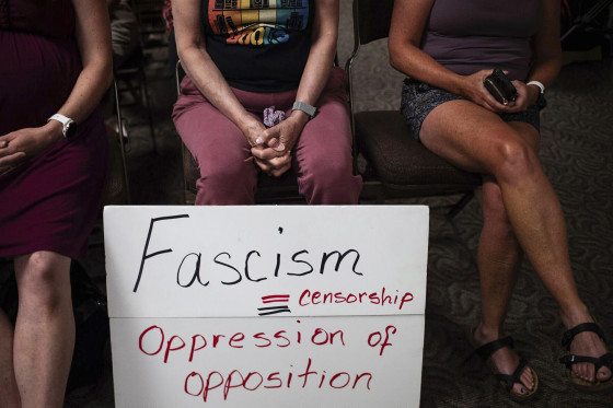 People sit with a sign at a Campbell County Library Board meeting