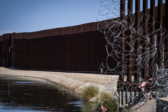 A man walks between a canal carrying water from the Colorado River and a border wall separating San Luis Rio Colorado, Mexico with San Luis, Ariz., on Aug. 14, 2022, in San Luis Rio Colorado, Mexico.