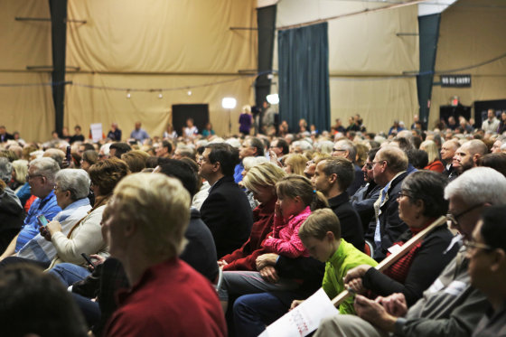 An auditorium is filled with people sitting in chairs, listening to an unseen speaker