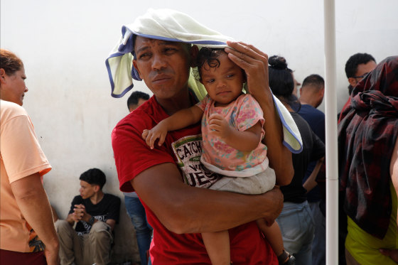 A migrant and his toddler daughter cover themselves from the sun.