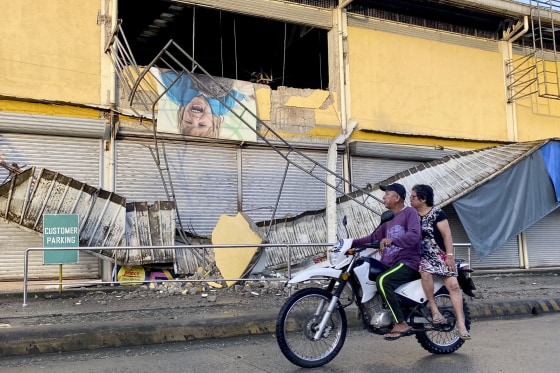 Image: A motorcycle passes by a partially damaged grocery store