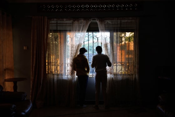 Two shadowed people look out of window , while adjusting curtains