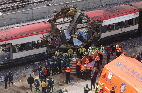 Rescue workers cover up bodies at the damaged passenger train in Madrid, Spain