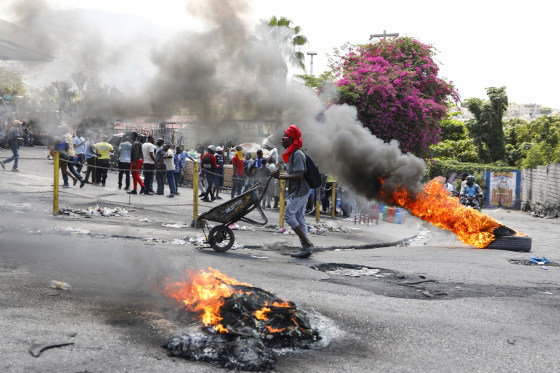 A man pushes a wheelbarrow past burning tires
