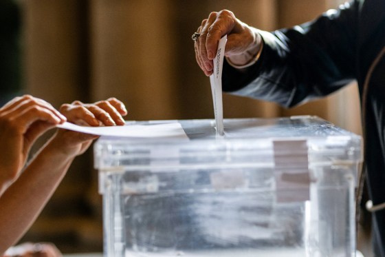 Two voters submit their ballots in a ballot box
