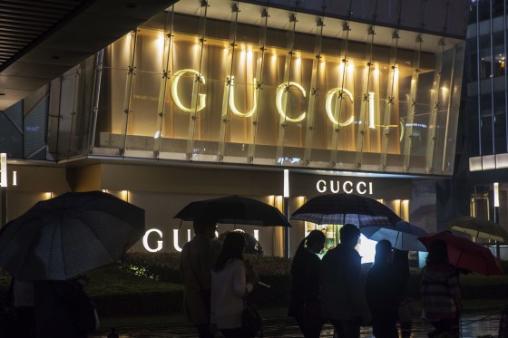 Pedestrians holding umbrellas walk past a Gucci luxury goods store, operated by Kering SA, at night in the Lujiazui district of Shanghai, China.