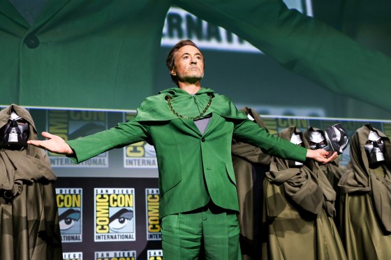 Robert Downey Jr. stands onstage with his arms outstretched, wearing a fully green suit