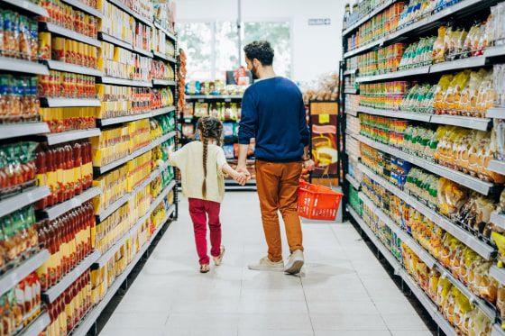 Father and daughter shopping at grocery store, they are holding hands while walking down the snack aisle.