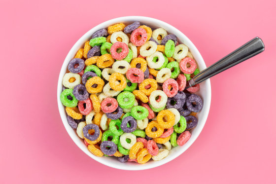 Colored breakfast cereal in a bowl on a pink background, flat lay.