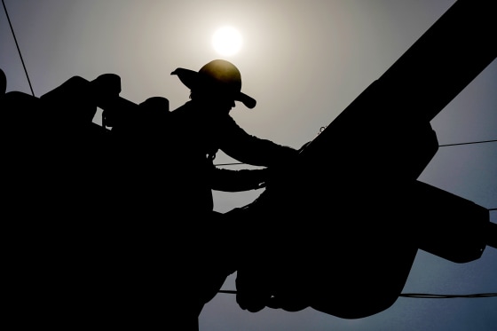 Image: A linesman works on power lines under the morning sun